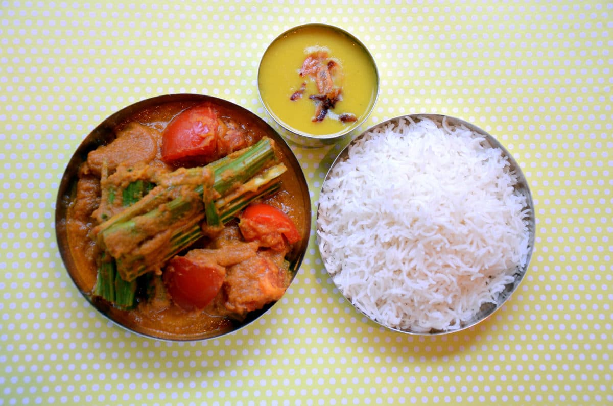 Bow of fish and drumstick curry beside a bowl of fluffy white rice.