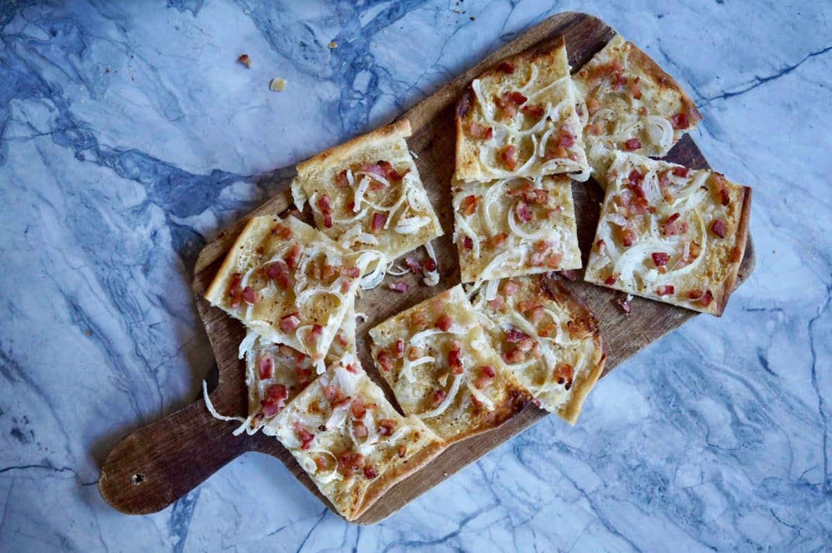 Flammkuchen slices served on a wooden cutting board.