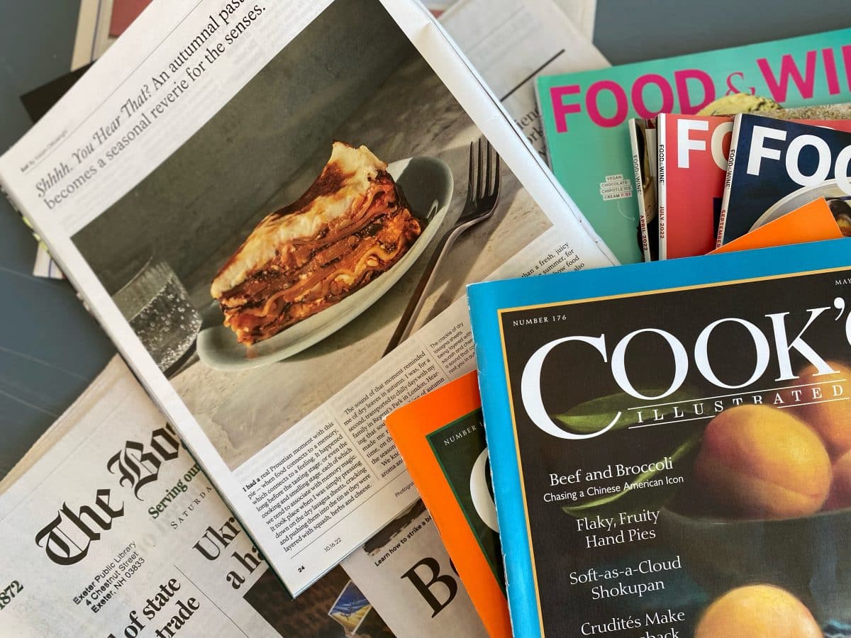 An array of food-related publications including a slice of lasagna on a newspaper.