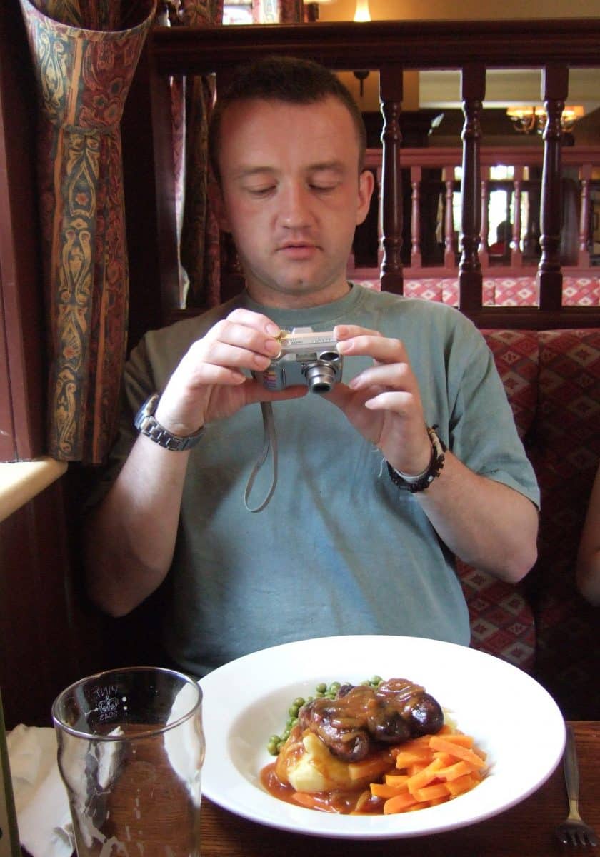 Man at a restaurant table taking a photo of his meal