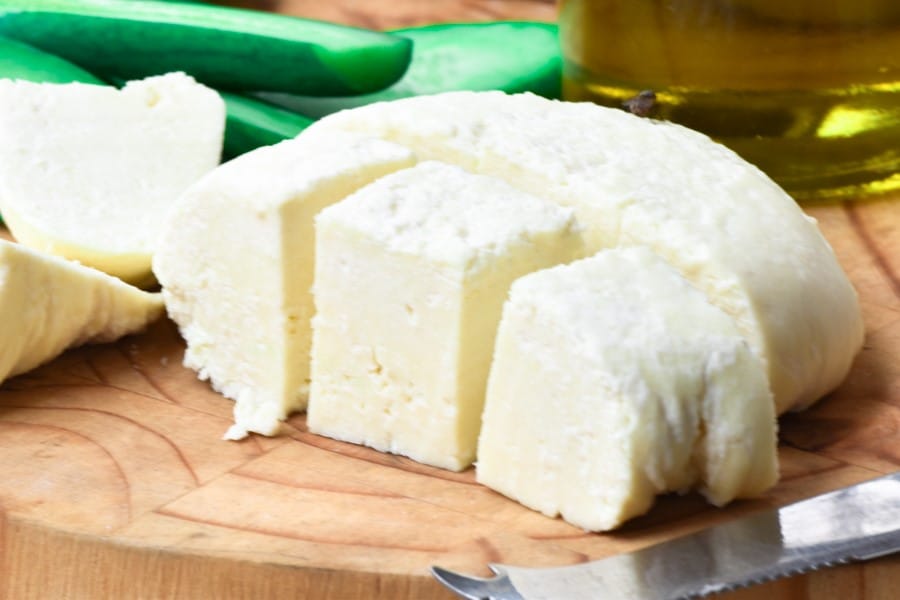 White cheese slices on a wooden board with olive oil.