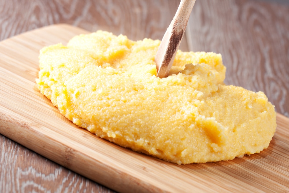 Pile of freshly made polenta on a wooden board with a wooden spoon