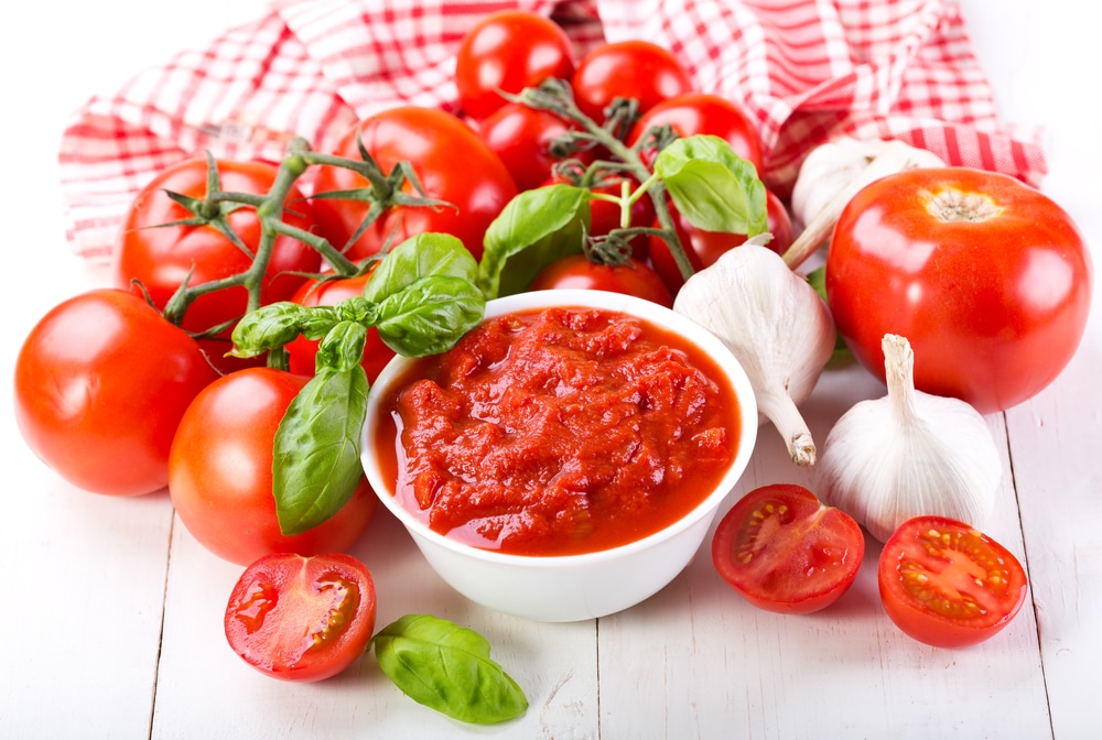 Bowl of tomato sauce surrounded by fresh vegetables on a white wooden table