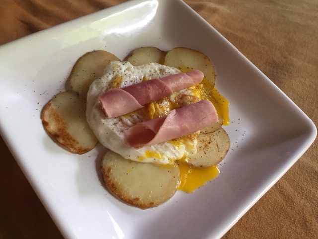 Plate showing fried potatoes, a fried egg, and slices of ham on top.