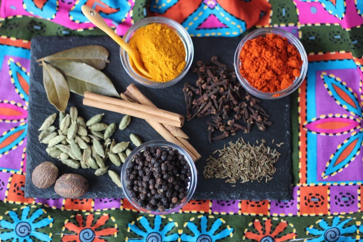 Assorted spices including turmeric, cloves, and bay leaves on a cloth.