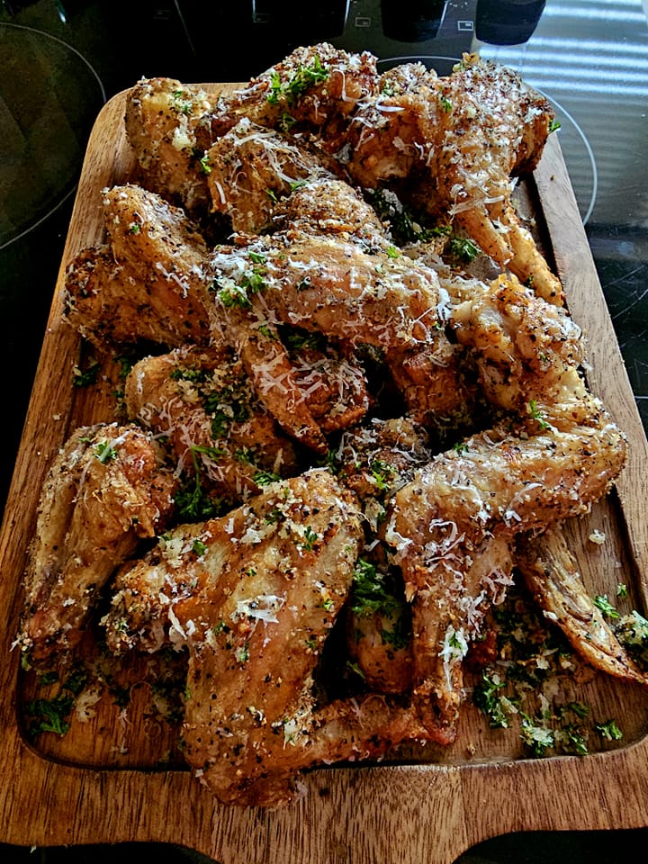 Delicious garlic pepper parmesan chicken wings on a wooden board.