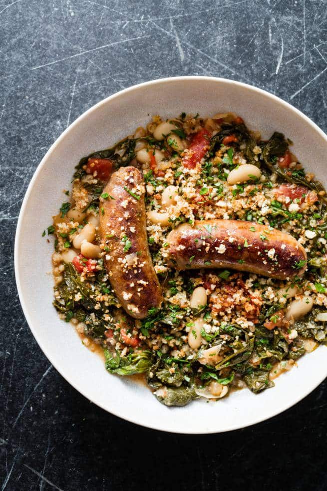 A bowl of garlic sausage and white beans with mustard greens.
