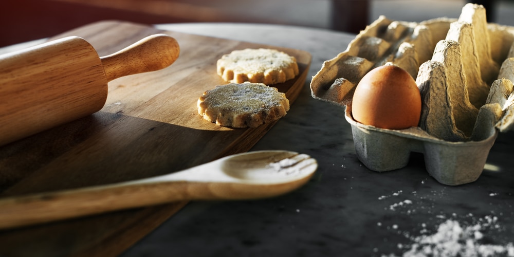 A wooden board with goat cheese and chive cookies, eggs, and a rolling pin.