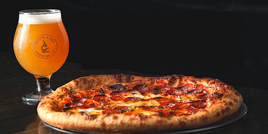 Gourmet pizza next to a glass of pale beer.