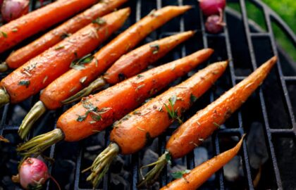 Grilled carrots garnished with fresh herbs on a grill.