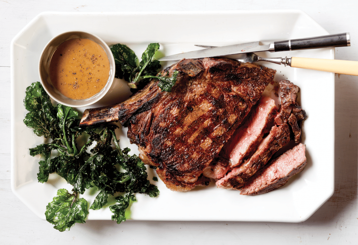 Close-up of grilled ribeye steak with West African sauce and green veggies.