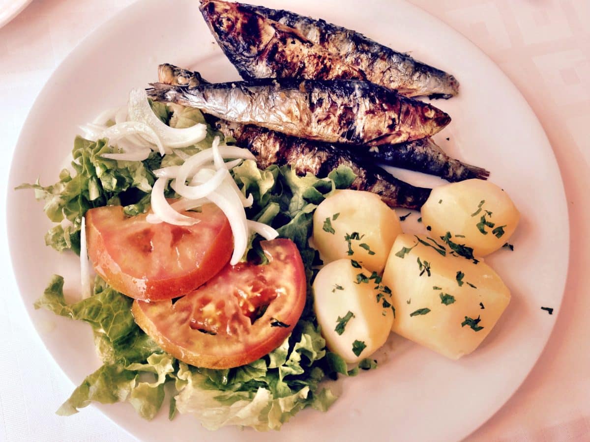 Plate of grilled sardines served with potatoes and salad.