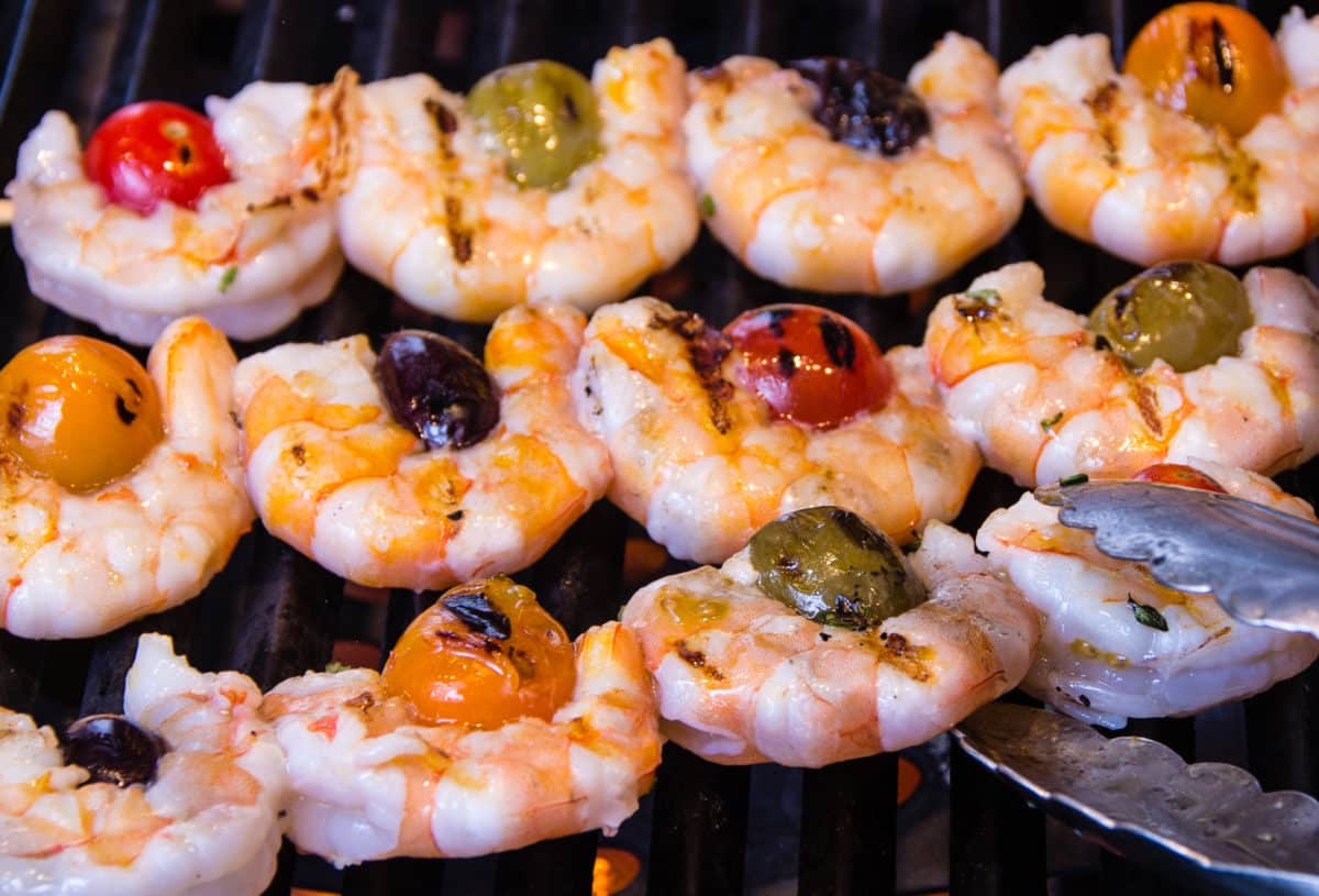 Skewers of shrimp, tomatoes, and olives grilling