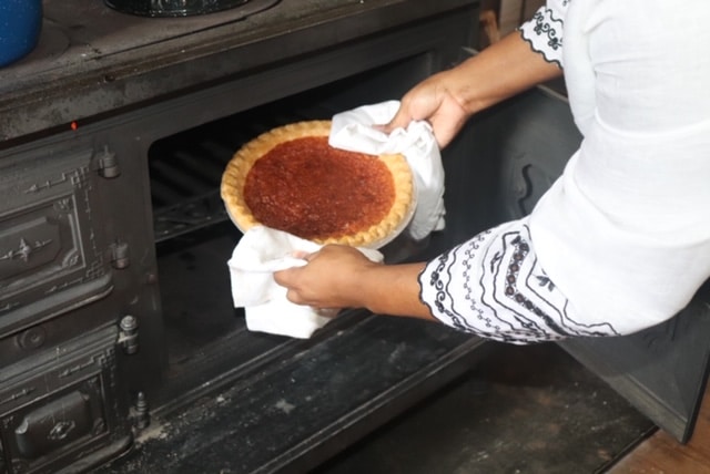 Close-up of a hand pulling a freshly baked pie from an oven.