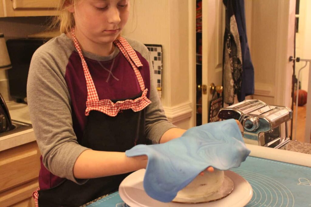 Young girl working with blue fondant on a kitchen table.