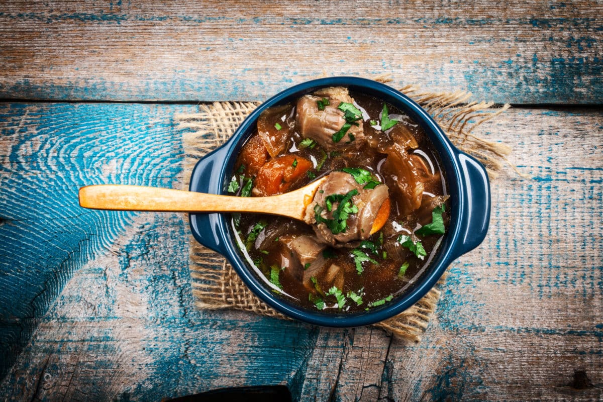 Delicious meat stew with vegetables and herbs served in a blue dish on a rustic wooden table.