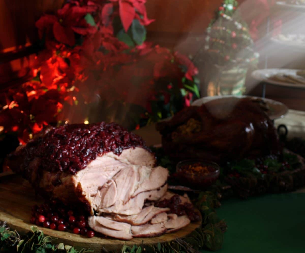 Cranberry glazed ham served on a wooden platter, set against a festive backdrop.