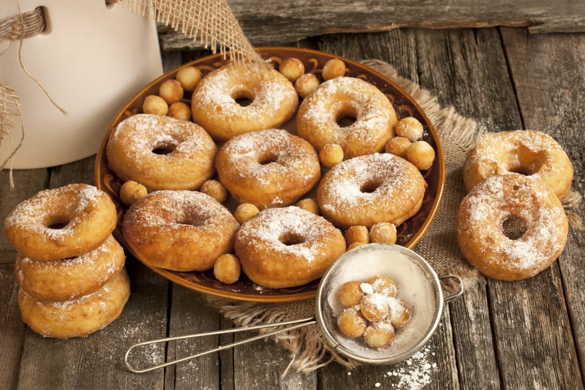 A plate of sugary homemade donuts with donut holes surrounded by hazelnuts.