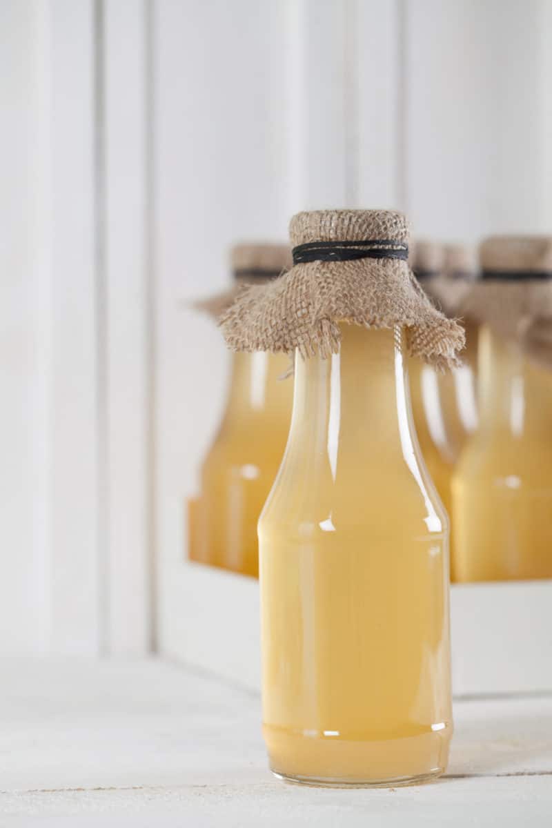 Bottles filled with yellow ginger syrup, sealed with cloth.