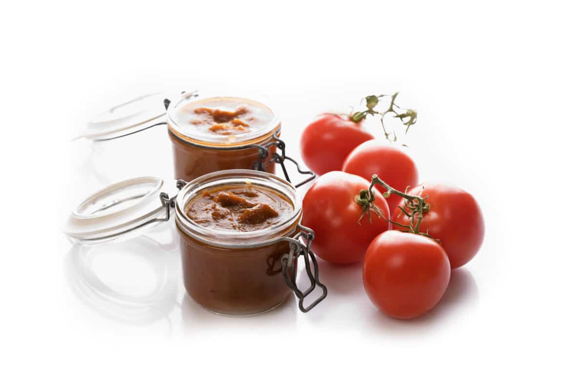 Jars of homemade ketchup with fresh tomatoes