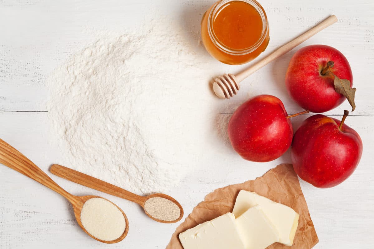 A spread of ingredients including flour, honey, apples, butter, and sugar for making a honey pie.