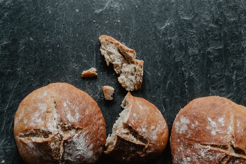 Close-up of a homemade Irish soda bread loaf with raisins on a black stone surface.