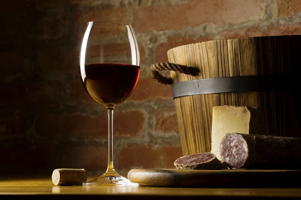 Cutting board with Italian food, red wine, hard cheese, and sausage in a rustic setting