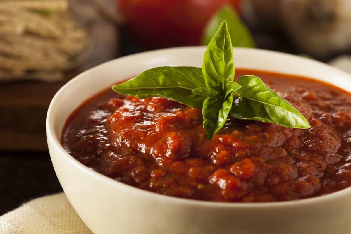 Close-up view of homemade red Italian marinara sauce garnished with fresh basil and garlic.