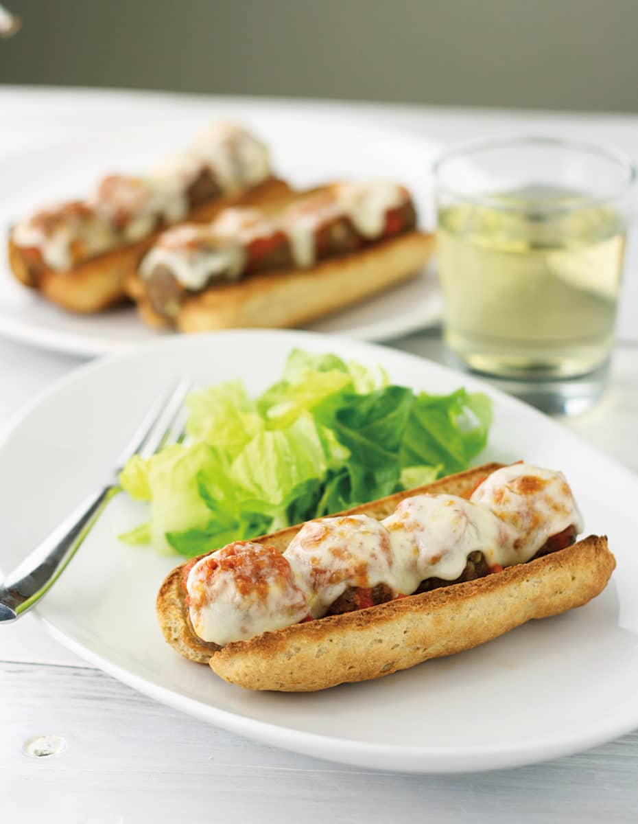 Plate with an Italian meatball sub served next to fresh green salad.