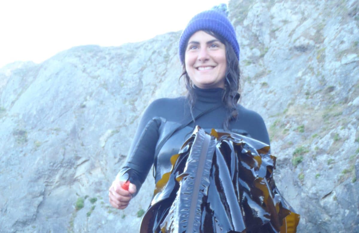Kacie Loparto in diving gear with harvested seaweed in a coastal setting.