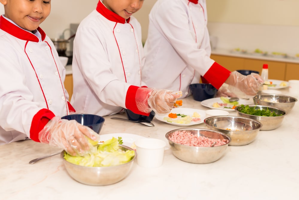 Young children in red and white uniforms preparing food in a cooking class.