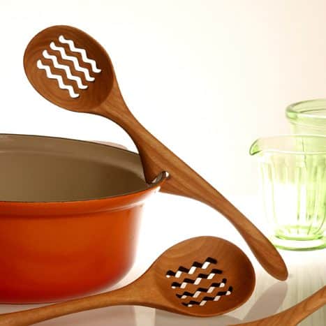 Wooden kitchen spoon resting on an orange pot next to a green measuring cup