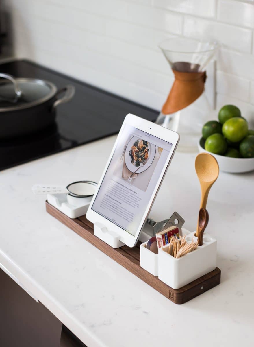 A wooden kitchen stand holding a tablet displaying a recipe, with cooking utensils alongside.