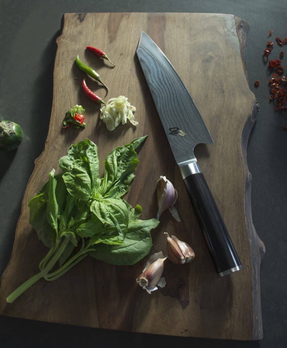 Knife placed on a wooden cutting board with basil and lemongrass