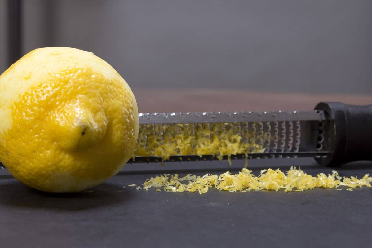 Fresh lemon zest grated on a black surface next to a zester.