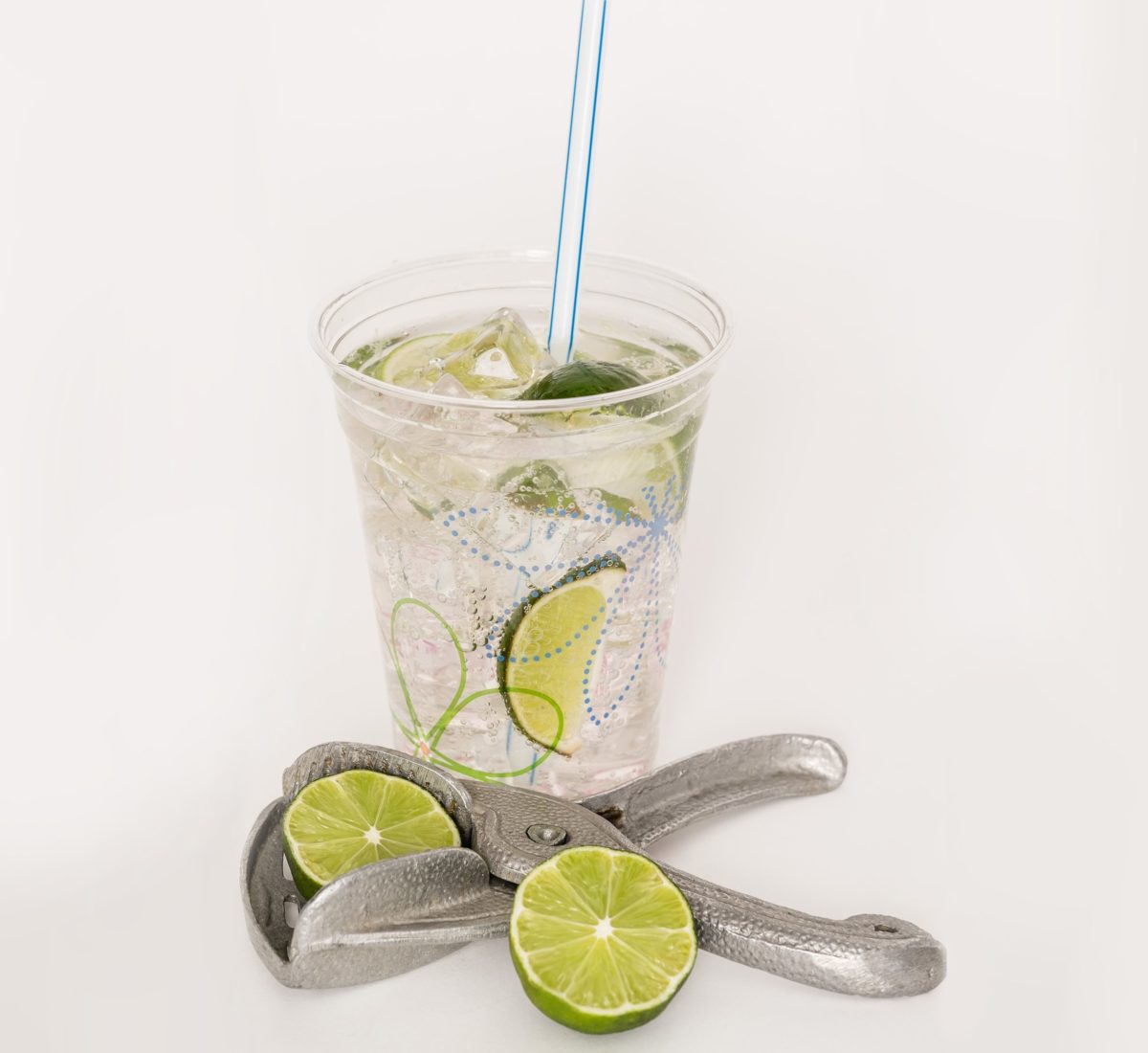 Clear drink with lime slices and a straw in a plastic decorated glass