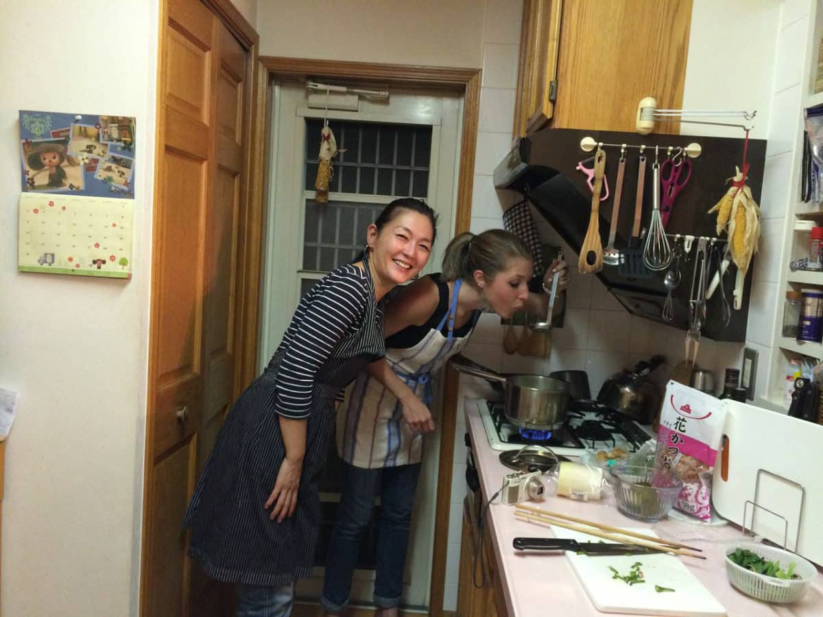 Two women in aprons smiling and preparing food in a well-equipped Tokyo kitchen.
