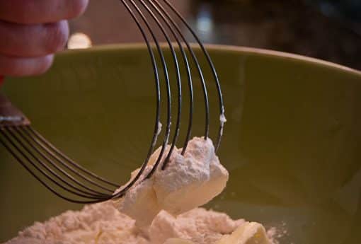 A whisk stirring flour and butter in a bowl for pie crust preparation.