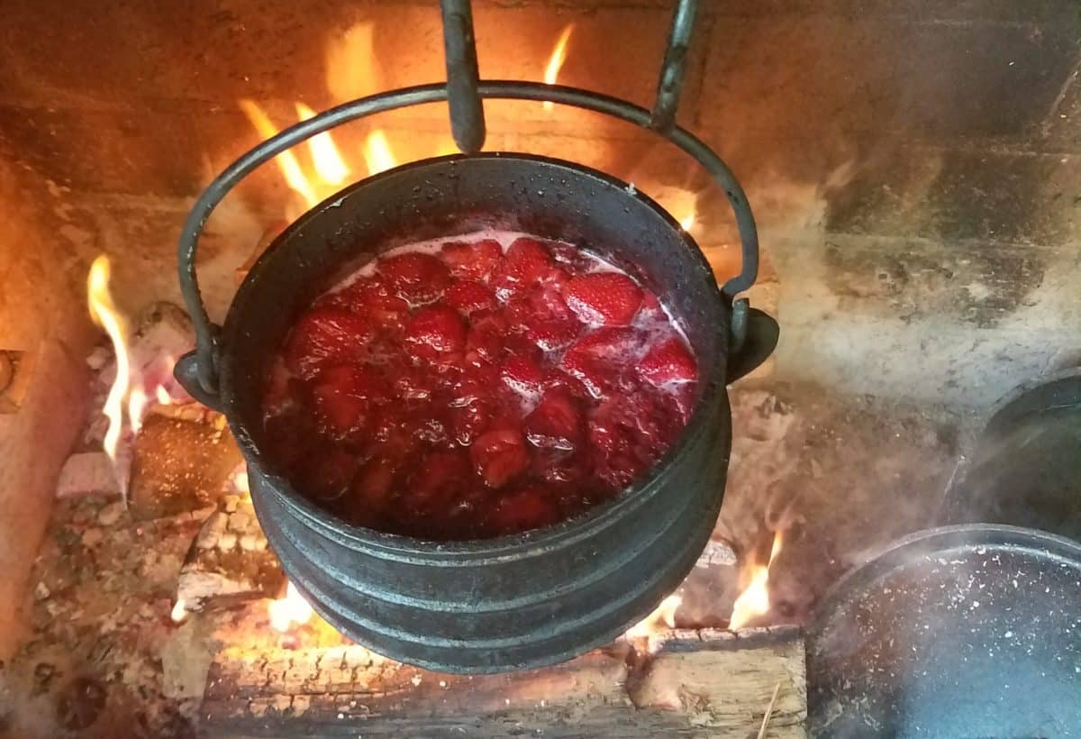 Fresh strawberries boiling in a cast iron pot, suspended over a wood fire.