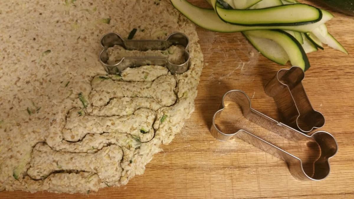 Bone-shaped cookie cutters on a mix with zucchini slices, used for making dog treats.