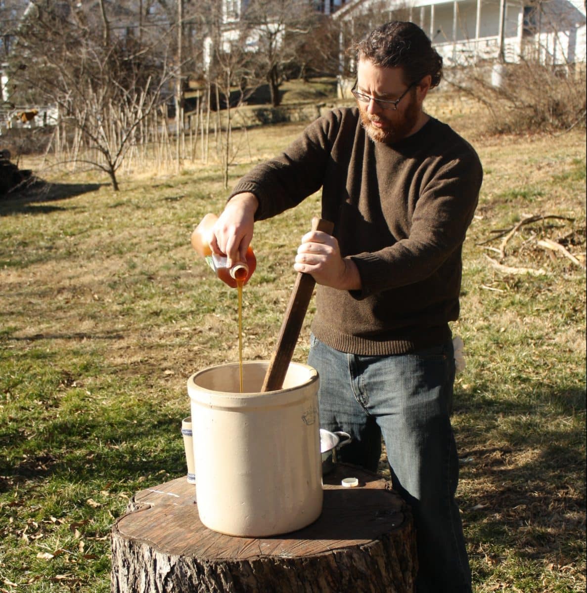 Man pouring a liquid into a container while making mead outdoors.