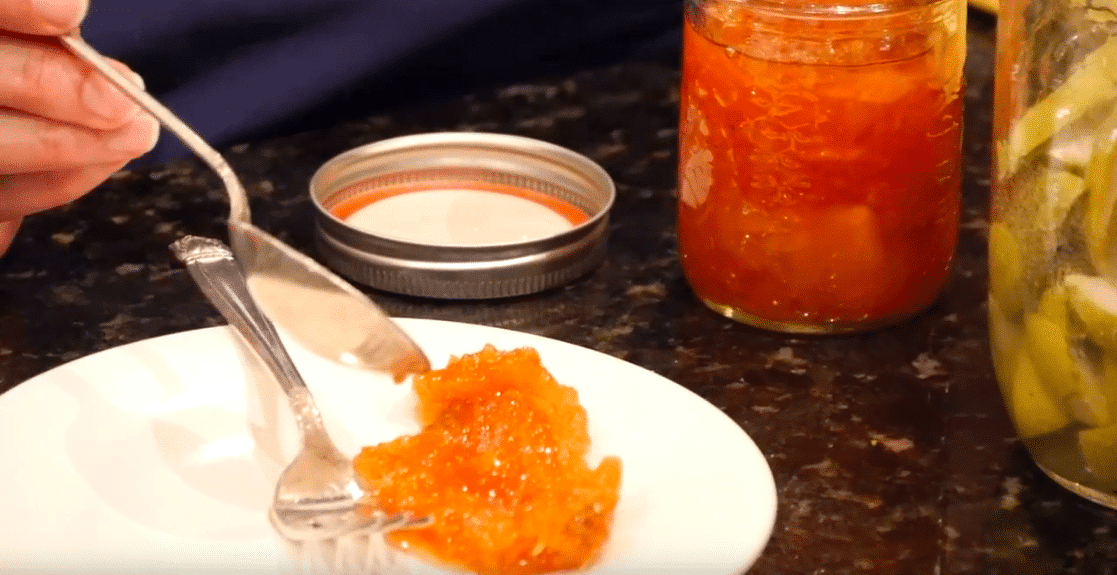 Serving of mango chutney next to a jar on a dark countertop