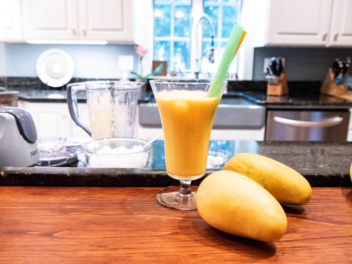 Mango lassi served in a tall glass with two straws