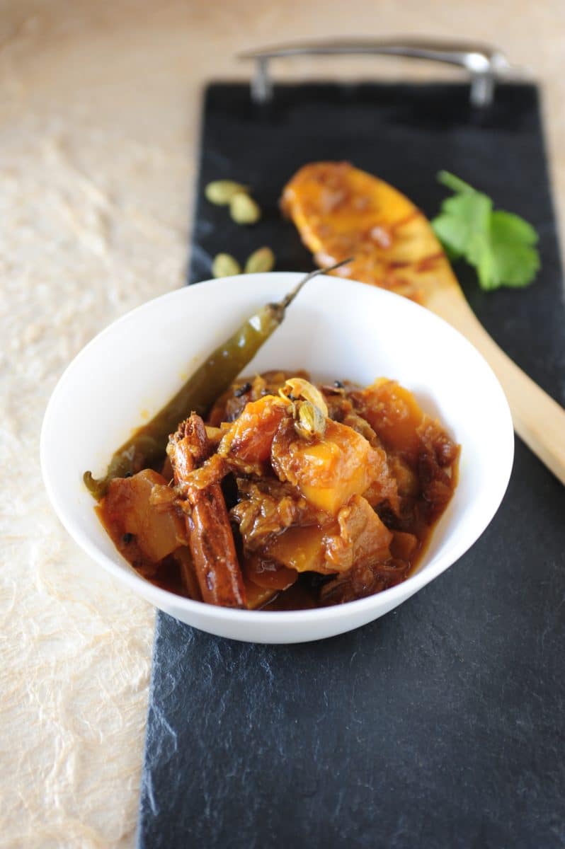 A bowl of Keri Kanda Mango Stew with onions and a garnish, served with a sliced and grilled mango on the side.