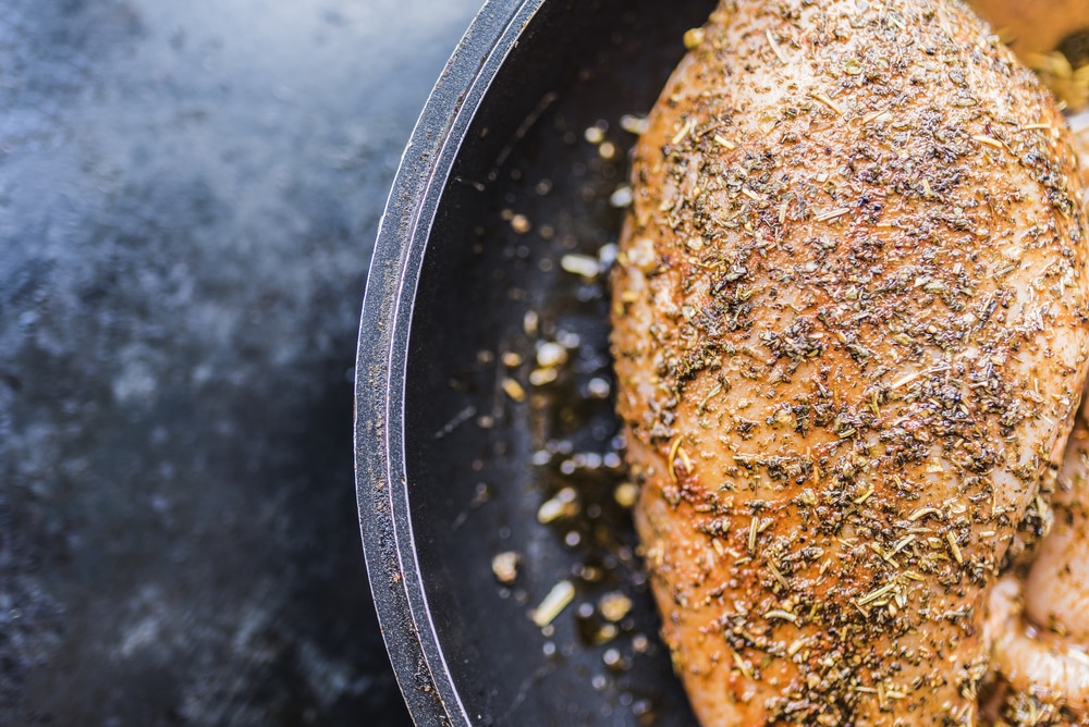 Herb-marinated chicken breast sizzling in a cast-iron frying pan.