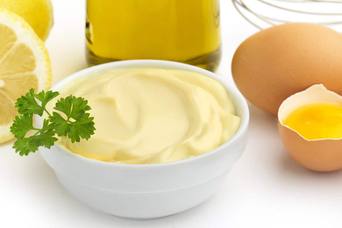 Close-up view of mayonnaise in a bowl with lemon and egg nearby.