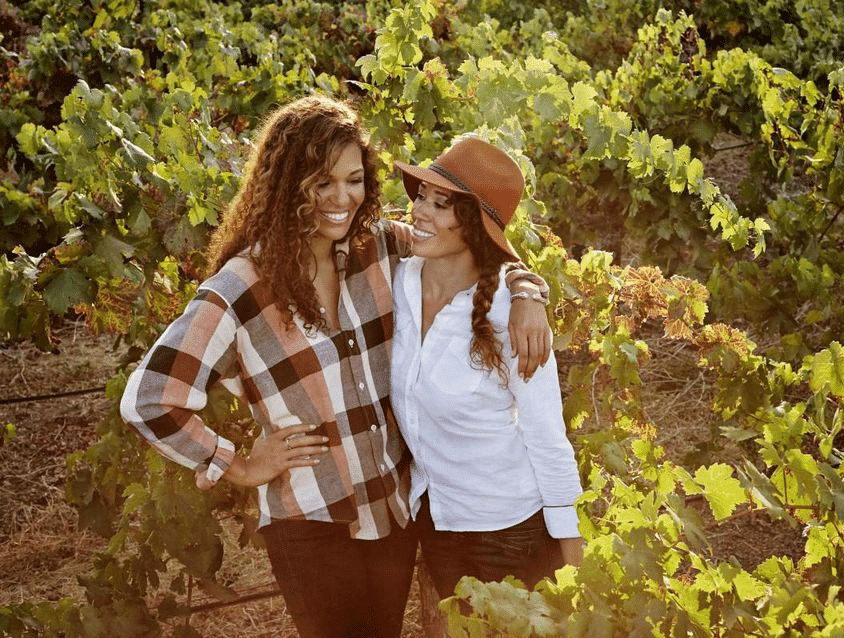 Two women laughing together in a vineyard.