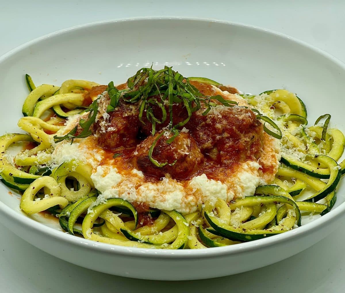 Meatballs in tomato wine sauce, served with fresh ricotta and zucchini noodles.