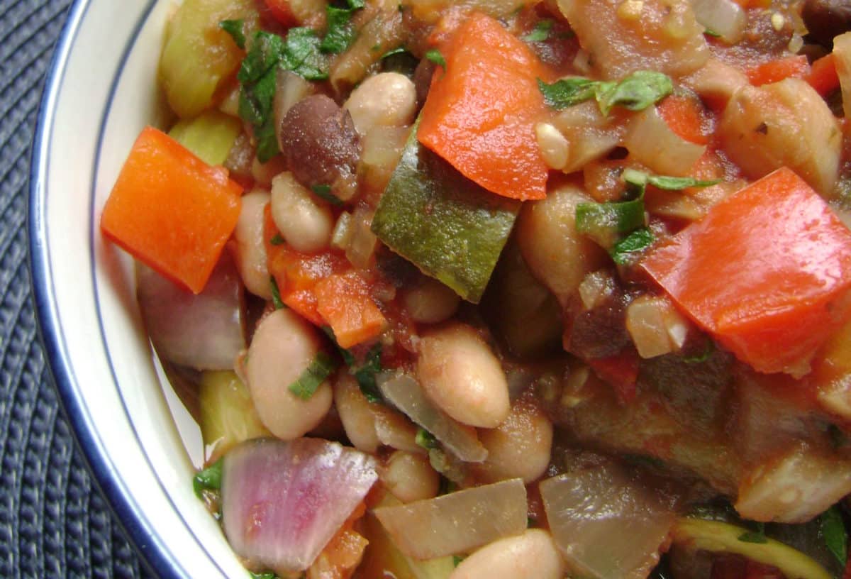 A close-up view of a Mediterranean stew with vibrant vegetables, beans, and fresh herbs.