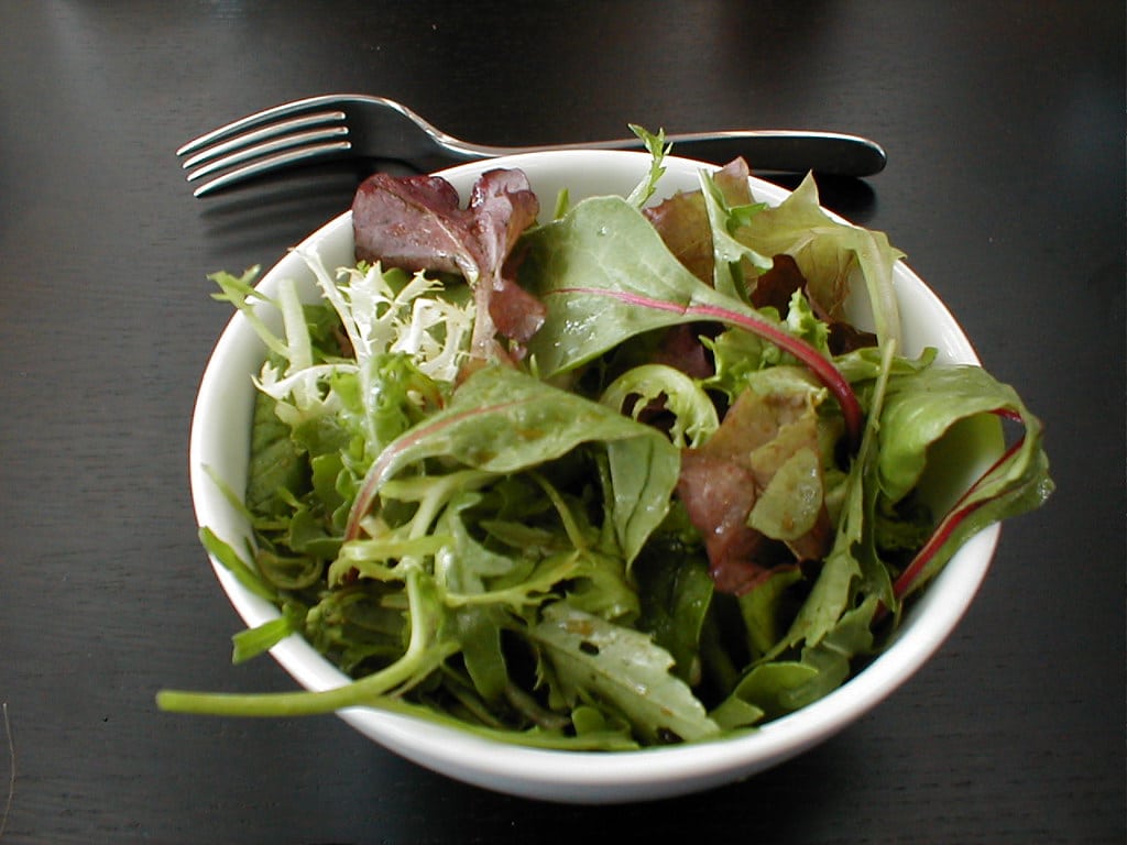 Fresh mesclun salad in a white bowl with a fork.